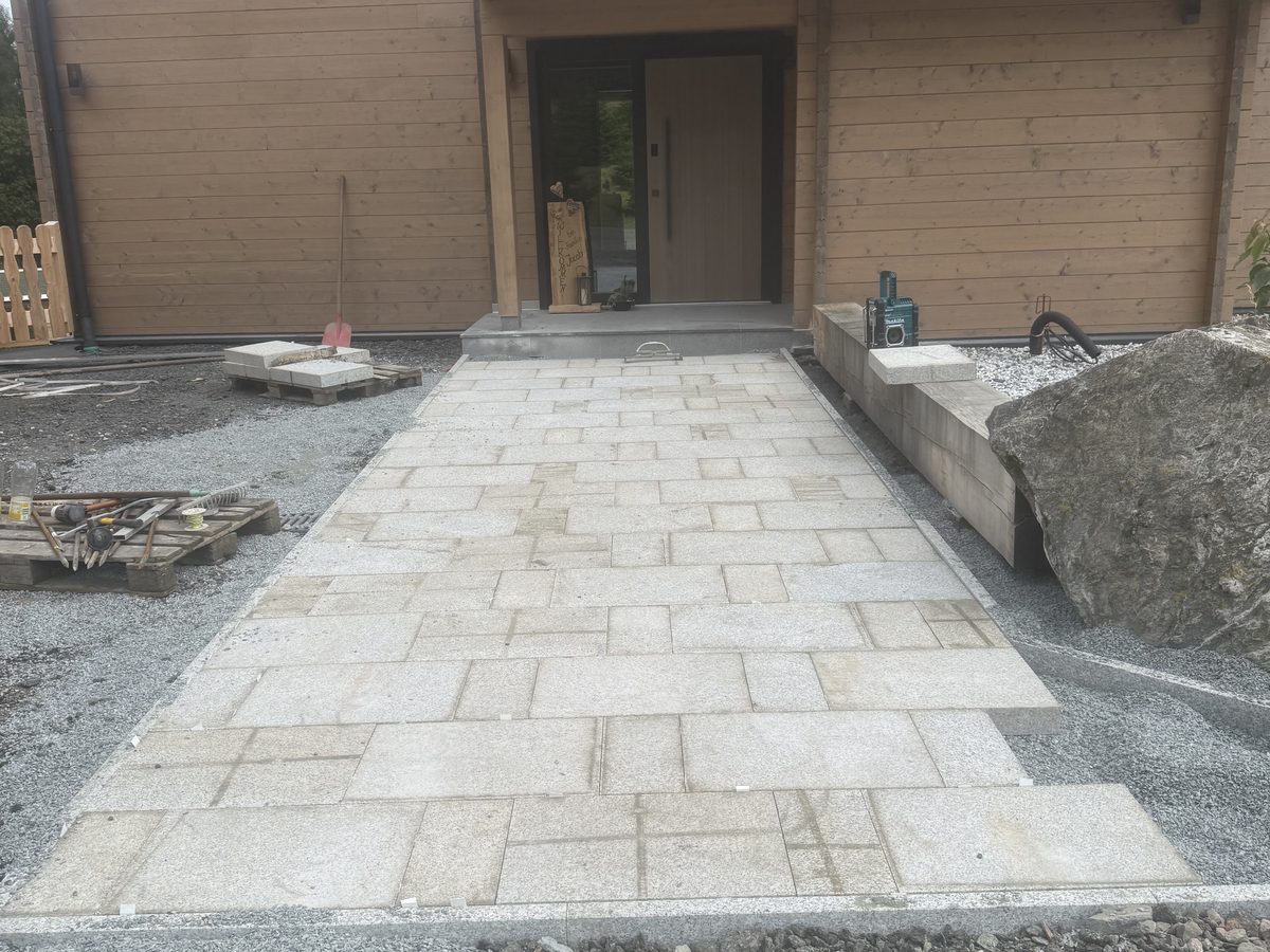 Neu gepflasterter Weg aus Natursteinplatten vor einem Holzhaus
