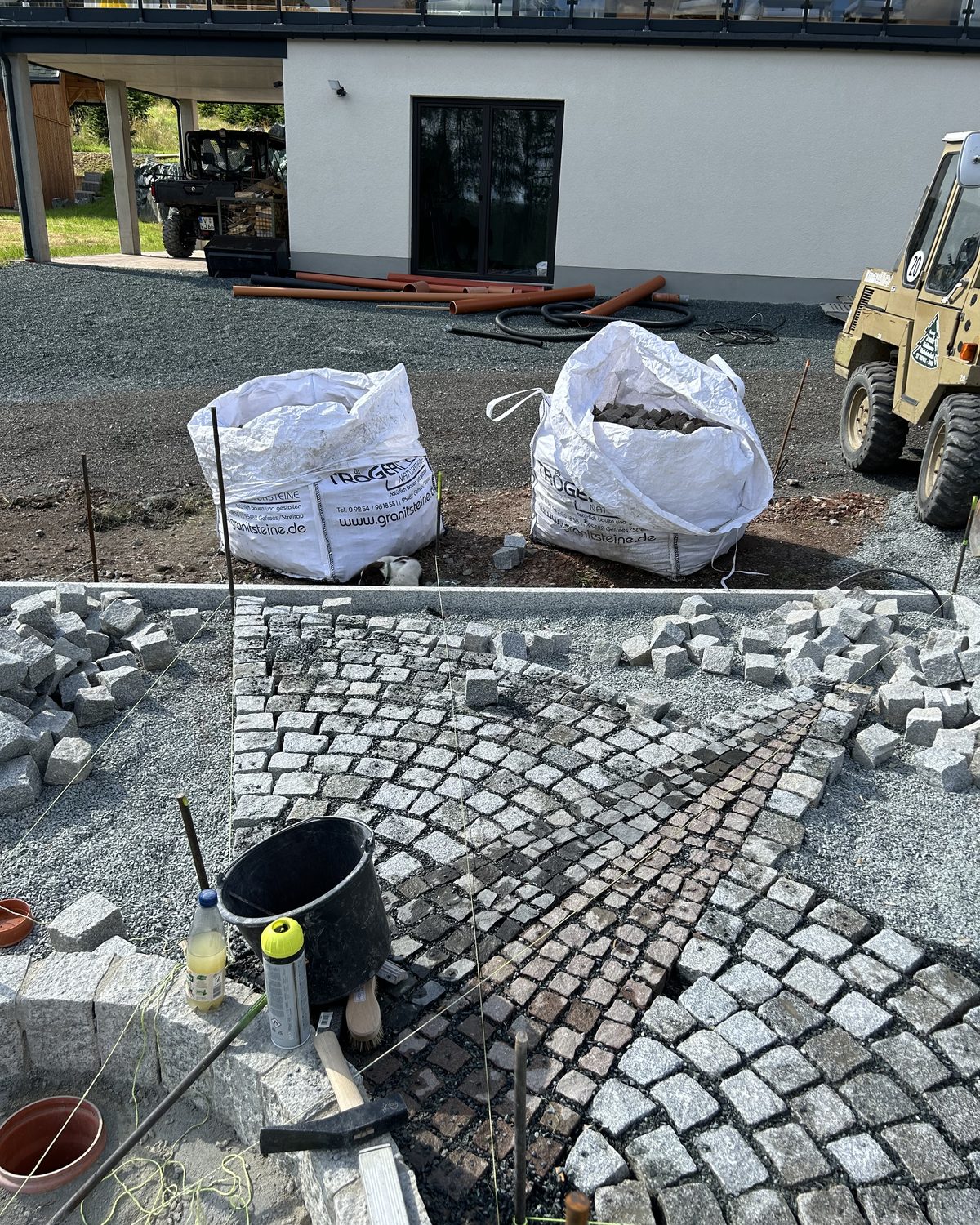 Pflasterarbeiten auf einer Baustelle mit Werkzeug und Big Bags voller Pflastersteine