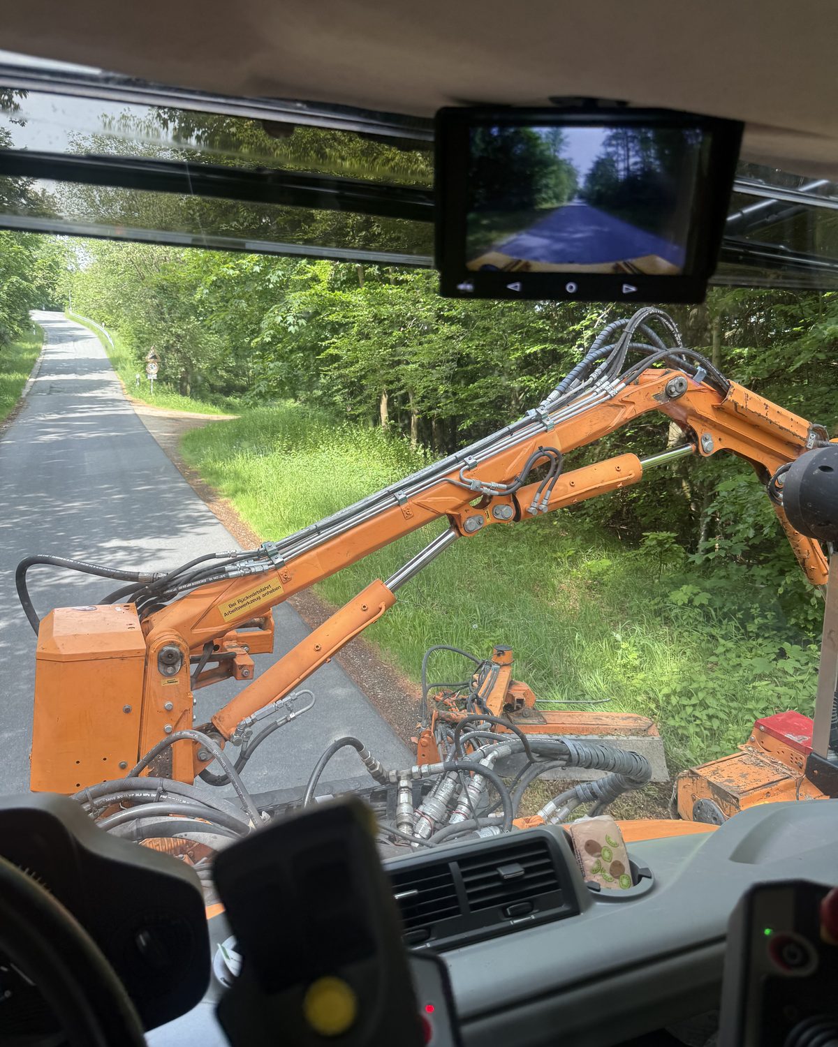 Blick aus der Fahrerkabine: Auslegermäher beim Mähen des Straßenbegleitgrüns