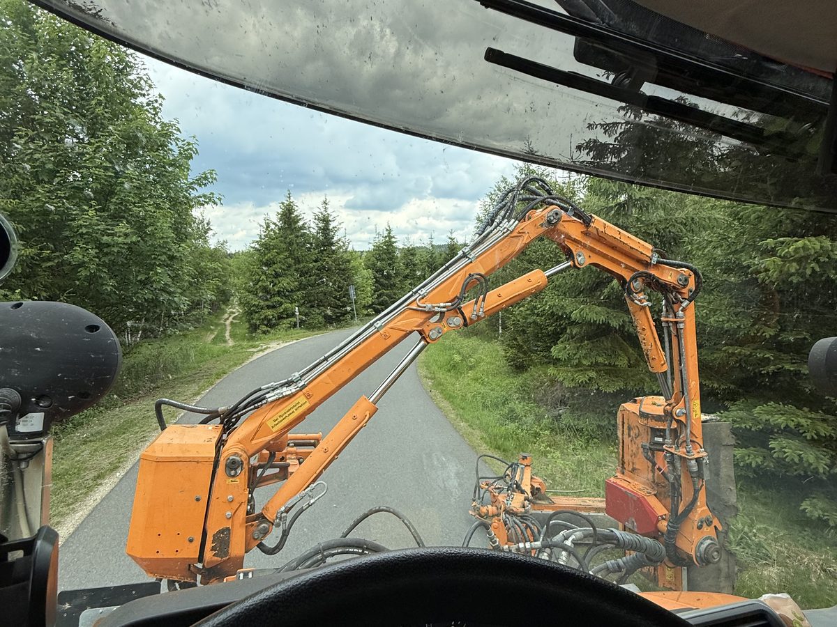 Blick aus der Fahrerkabine auf ein Ausleger-Mähgerät am Straßenrand