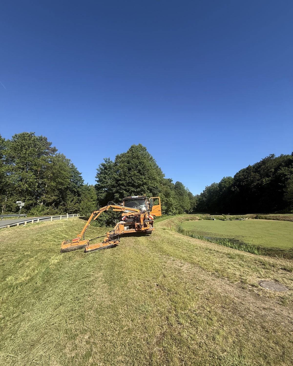 Unimog mit Auslegermäher beim Mähen einer Wiese