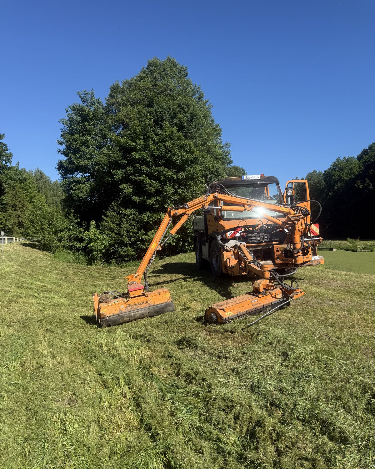 Unimog von NaturBalance mit Ausleger-Mulcher bei Mäharbeiten an einer Böschung