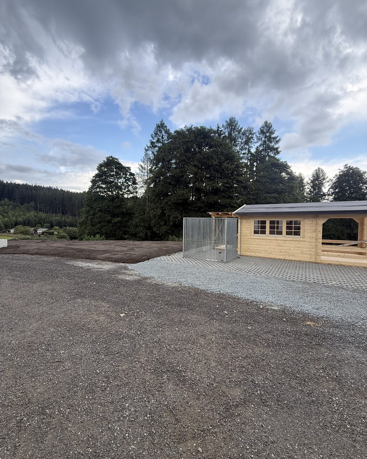 Neu angelegte Außenanlage mit Schotterflächen und Gartenhaus vor Waldrand